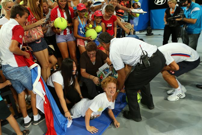 Novak Djokovic goes down on his haunches after an spectator barrier collapsed as he was signing autographs.