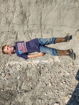 Liam Fisher lies next to the dinosaur discovery. His father texted this image to<strong> </strong>Lyson, a former classmate, who set the stage for the fossil's excavation.