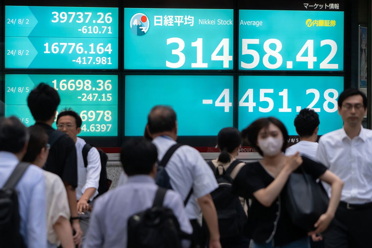 Pedestrians walk in front of monitors displaying the Nikkei 225 Stock Average figure outside a securities firm on August 5 in Tokyo, Japan.