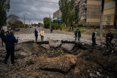 Local residents examine a crater following a missile strike in Dnipro, Ukraine, on October 10,