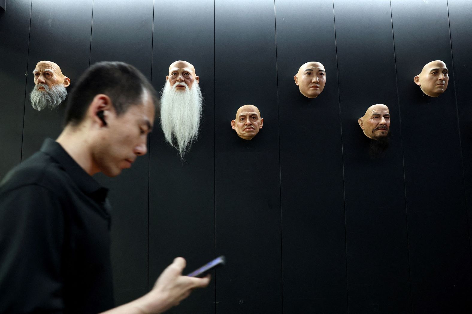 An employee at humanoid robot developer Ex-Robots checks his mobile phone as he walks past displays of robot heads in Dalian, China, on Thursday, June 6.