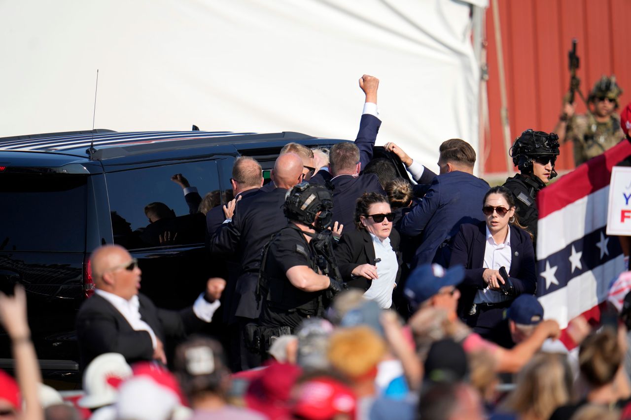 Trump raises a fist as he is helped into a vehicle and taken away from the rally. 