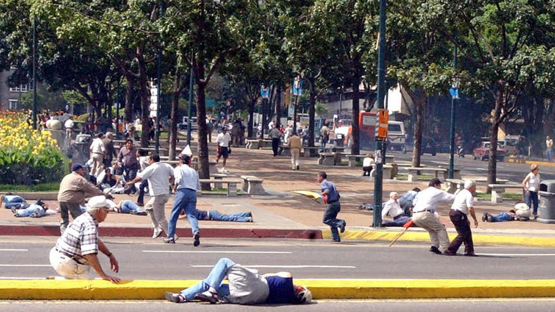 People try to take shelter from gunshots fired near Altamira Square in Caracas on August 16, 2004. At least three people were wounded by gunshots after Chavez supporters fired on opposition demonstrators, police said. A vote to recall Chavez as president failed on August 15.