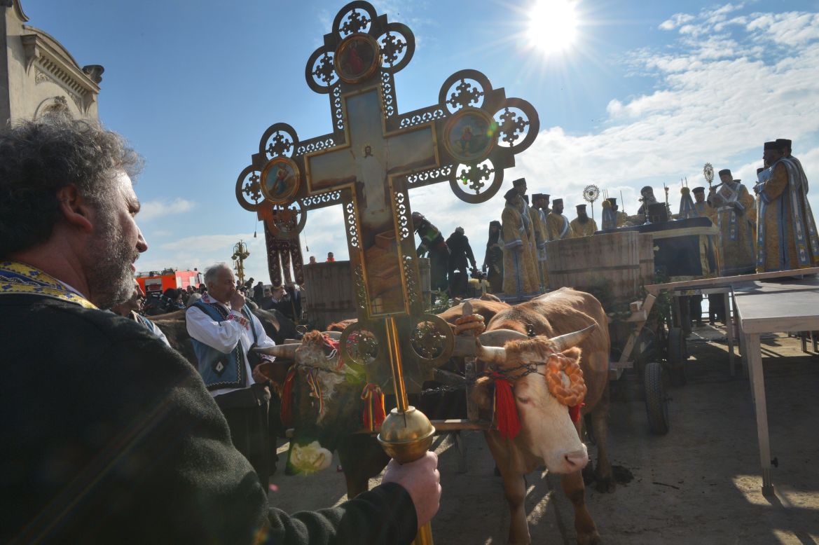 A priest holds a cross next to an ox-drawn cart transporting water to be consecrated during the Epiphany service in Constanta City on Sunday.