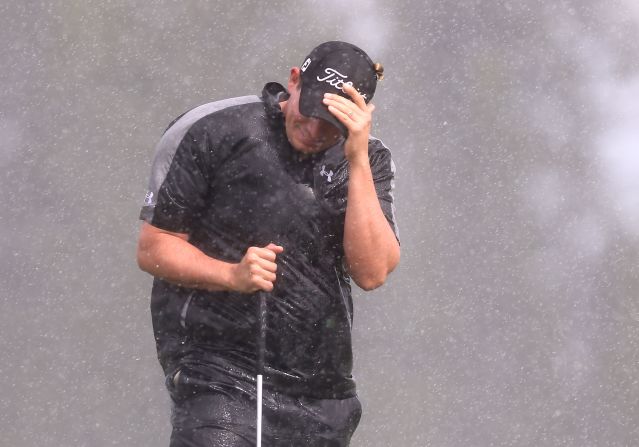 Scott Stallings shields himself from the wind and rain as he attempts to putt on the second hole green on Friday.