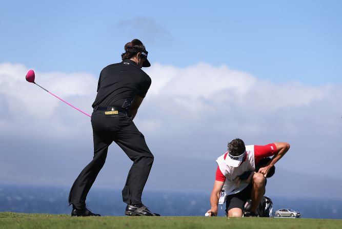 Masters champion Bubba Watson pretends to tee off as his caddy Ted Scott holds a finger on the ball to keep it from blowing away during Sunday's delayed opening round of the Tournament of Champions.