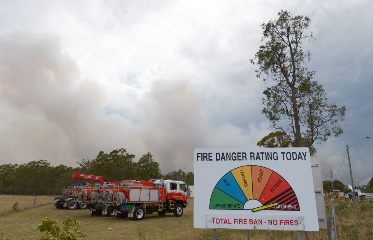 A fire danger rating sign set to catastrophic stands near fire trucks as smoke billows into the sky on the outskirts of Wandandian on January 8. On Tuesday afternoon, more than 130 fires were burning throughout NSW, according to the NSW Rural Fire Service.
