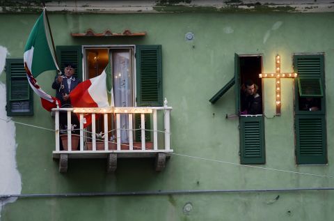 A man holds a flag on his balcony overlooking the port on the Italian island of Giglio on Sunday.