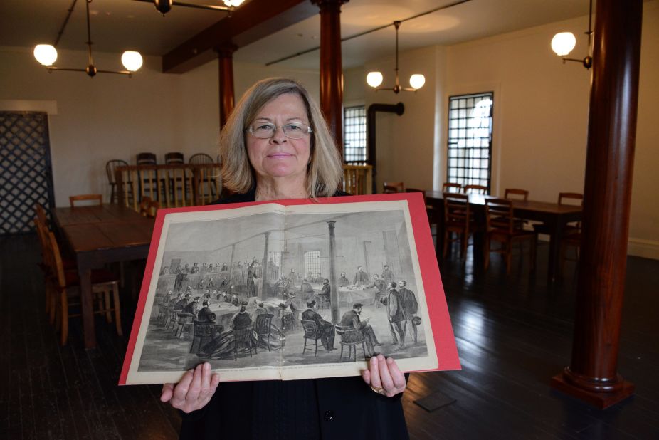 Susan Lemke, a librarian at the National Defense University, holds a depiction of the Lincoln assassination conspirators' trial, while standing in the restored courtroom in Washington where the trial occurred.