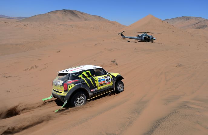 Nani Roma and co-driver Michel Perin of team Mini race through the desert with a helicopter nearby on January 18.