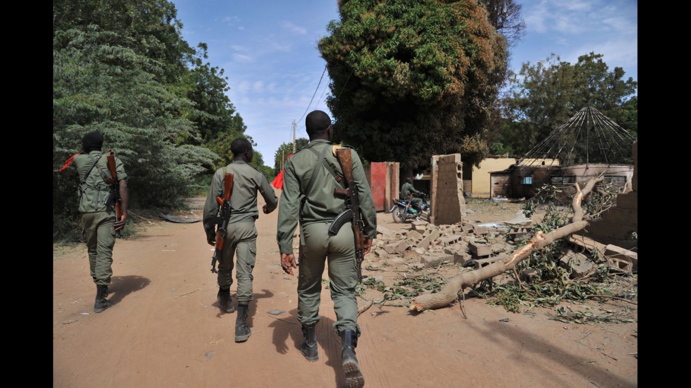Malian soldiers walk past destroyed army barracks as they patrol in Diabaly on January 22, 2013.