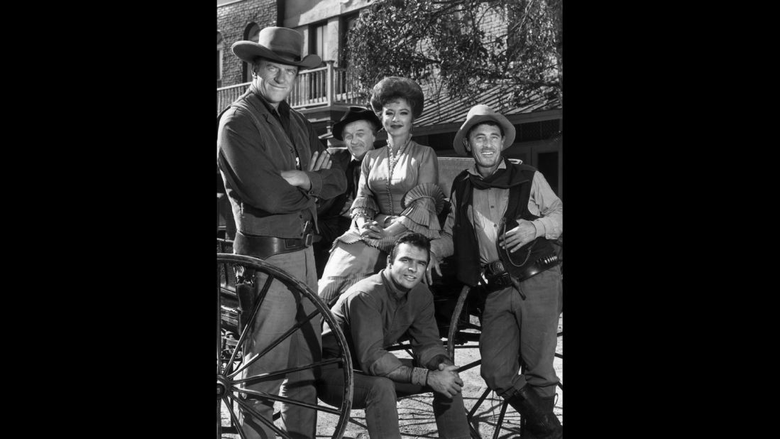 The cast of the hit TV show "Gunsmoke" poses around a wagon in 1962. Behind Reynolds, from left, are James Arness, Milburn Stone, Amanda Blake and Ken Curtis.