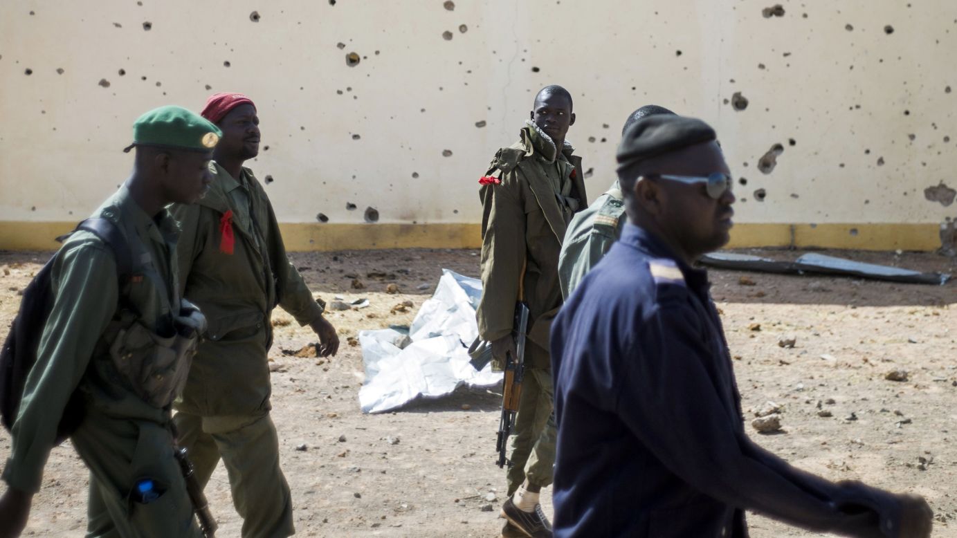 Malian soldiers walk past the bullet-riddled wall of a house in Konna on Saturday, January 26.