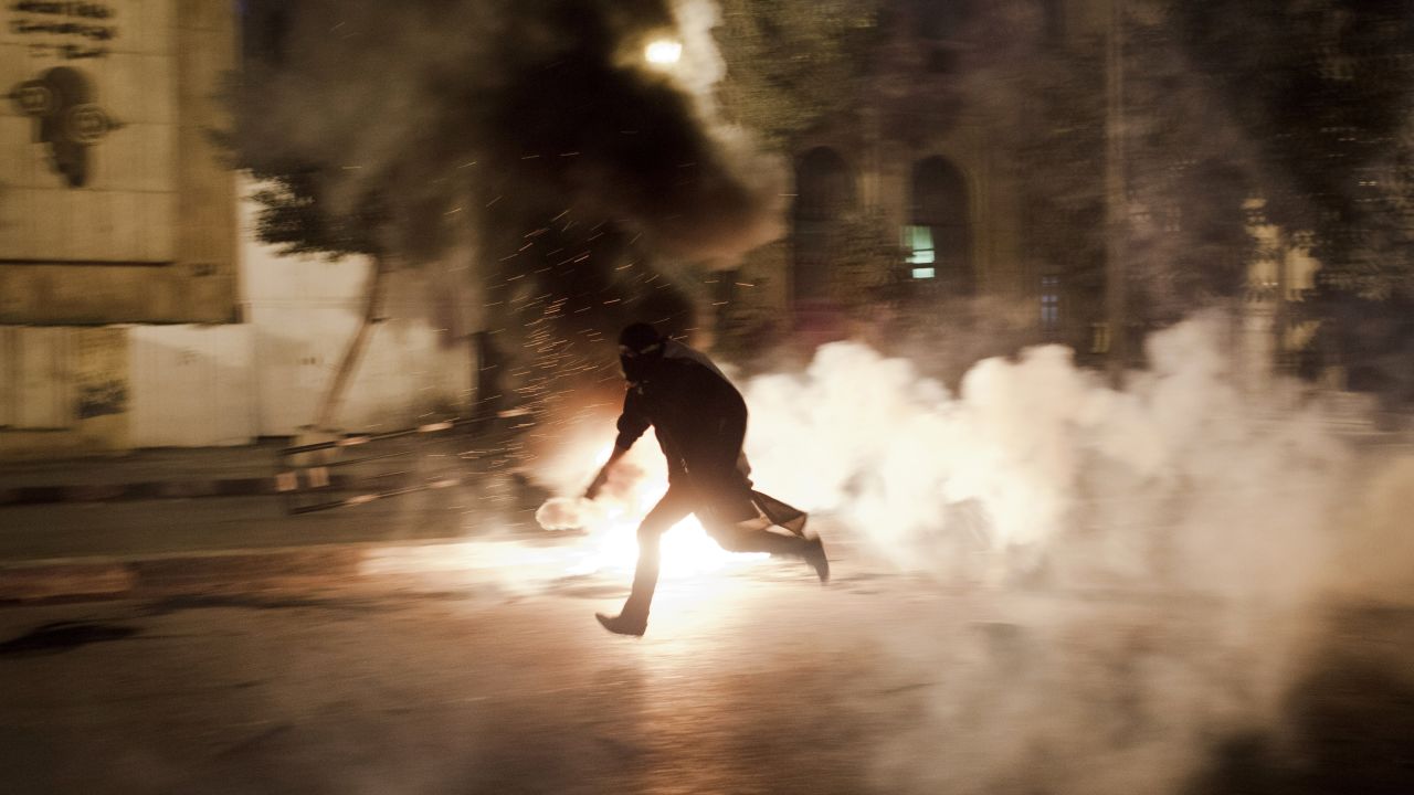 An Egyptian protester runs with a live tear gas canister toward Egyptian riot police on Saturday, January 26, in Cairo.