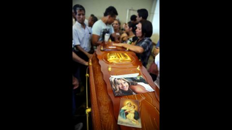 A coffin decorated with a photograph and image of the Virgin Mary is surrounded by mourners.