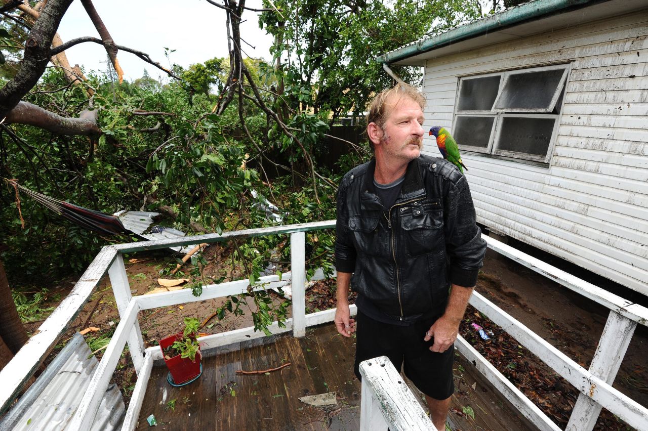 Andrew Cooney and his pet parrot, Jake, survey the uprooted trees outside his storm-damaged home in Bargara, Queensland.