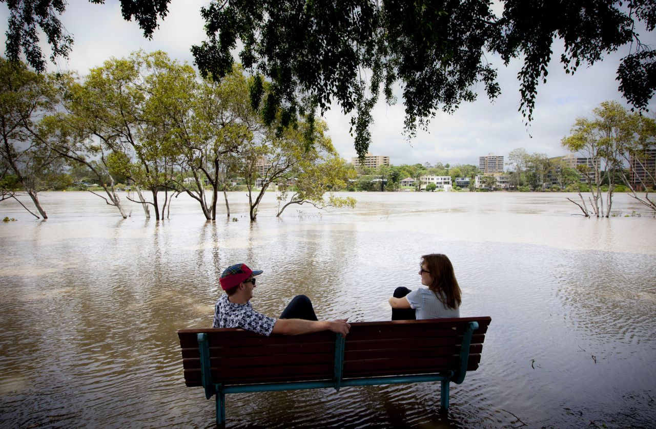 Peter Wison, left, and Beata Jaremko sit on a bench surrounded by floodwaters after the Brisbane River broke its banks on January 28.