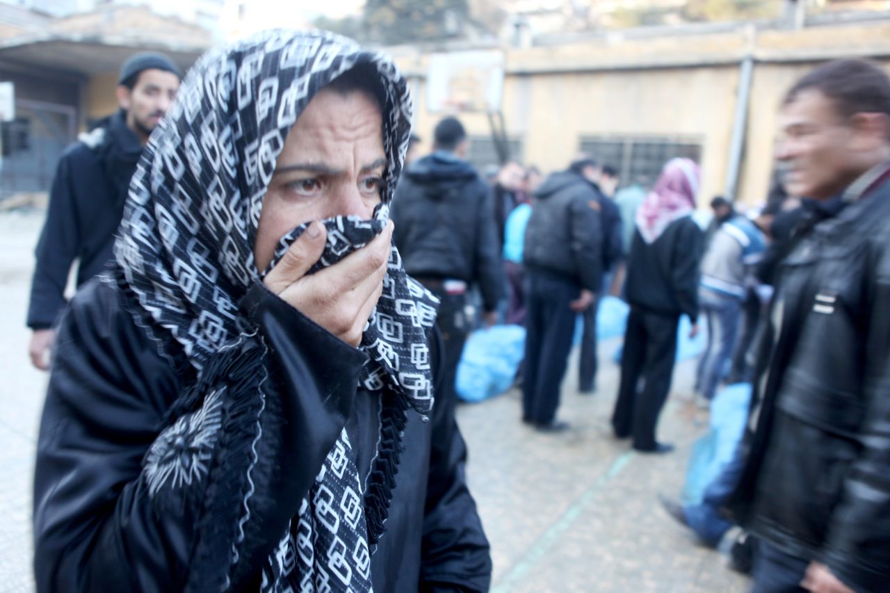 A woman covers her face as she walks through the lines of bodies on Tuesday.
