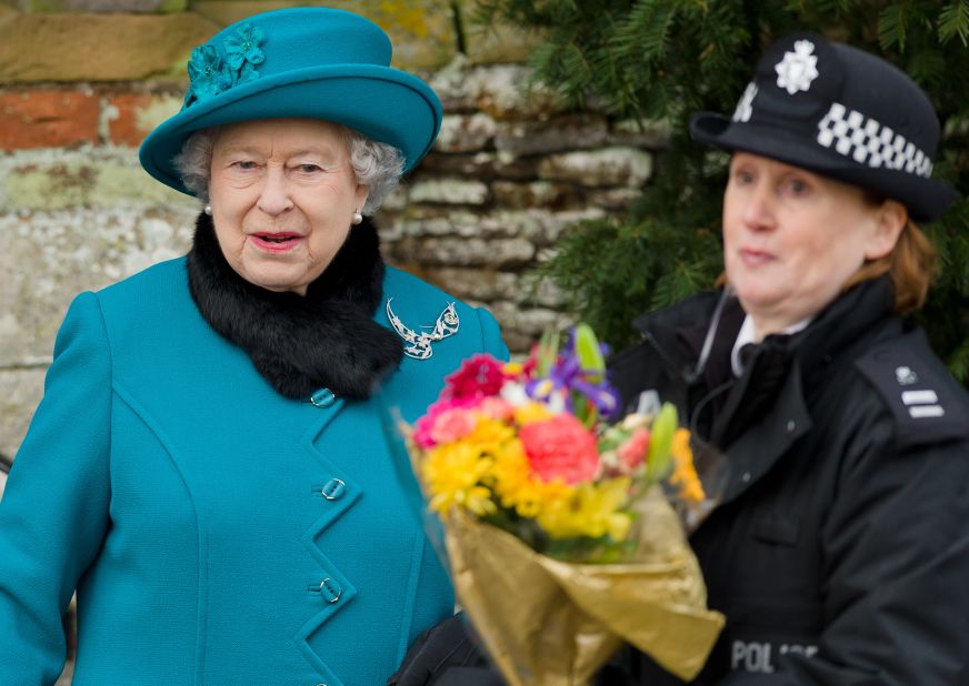 Britain's Queen Elizabeth II  hands a police officer some flowers she received from children as she leaves Christmas services at St. Mary Magdalene Church in Sandringham, Norfolk, England.