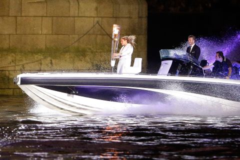 Beckham passes under London's Tower Bridge in a speedboat carrying the Olympic Torch in 2012.