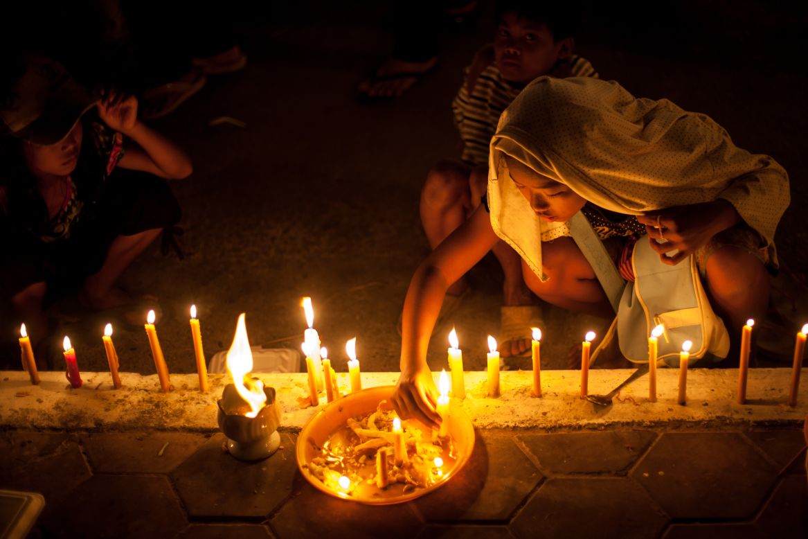 Young children light candles outside the Royal Palace on Thursday, ahead of a lavish funeral procession that saw his body carried from the palace to a funeral pyre in a nearby park.