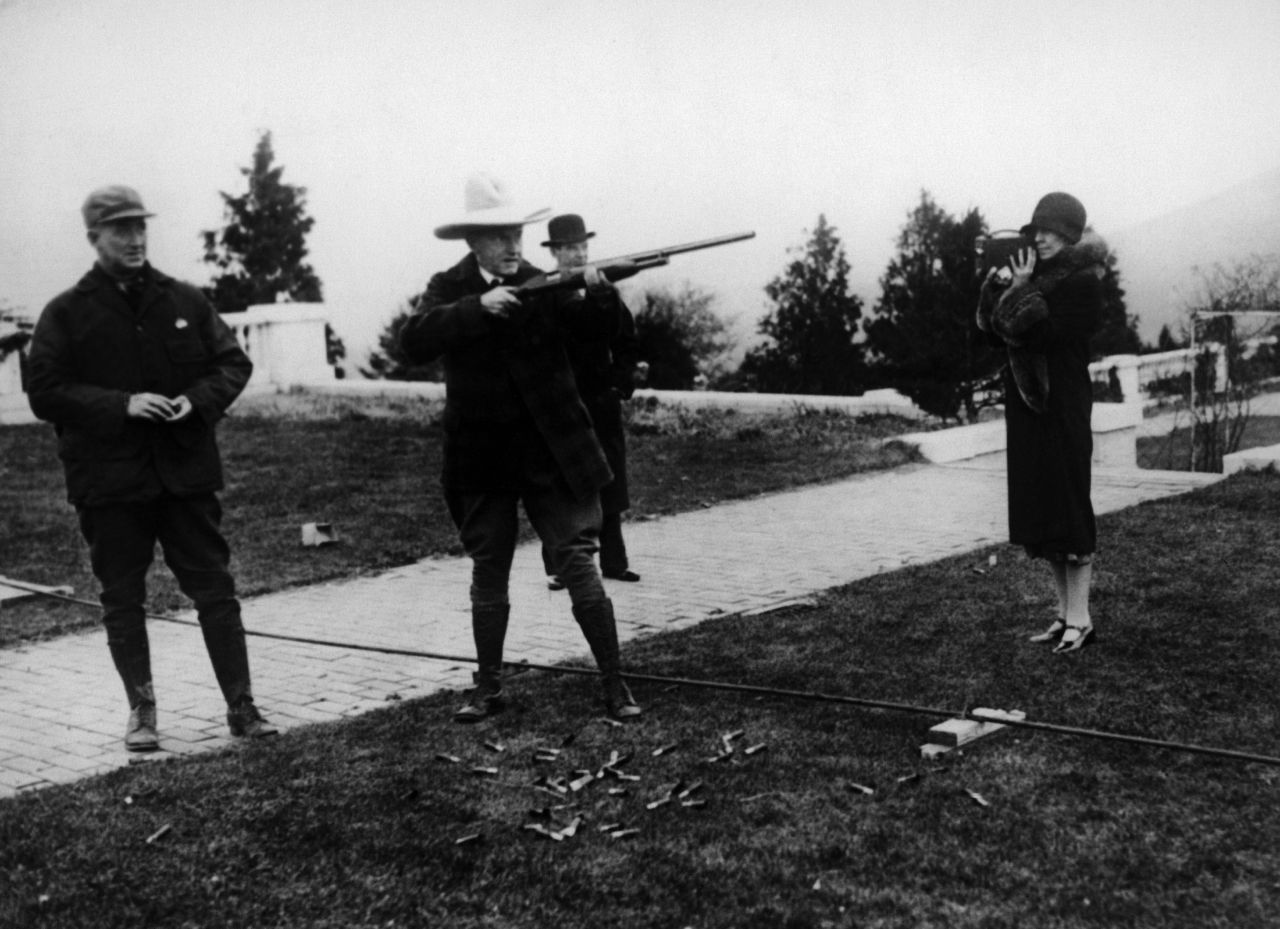 President Calvin Coolidge fires a gun as his wife, Grace Goodhue, photographs him circa 1925.