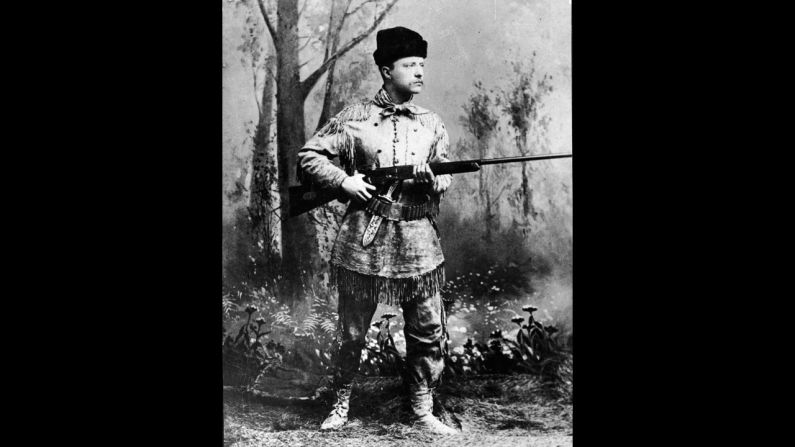 Theodore Roosevelt wields a Winchester rifle in this portrait taken in an artificial forest setting, circa 1900.
