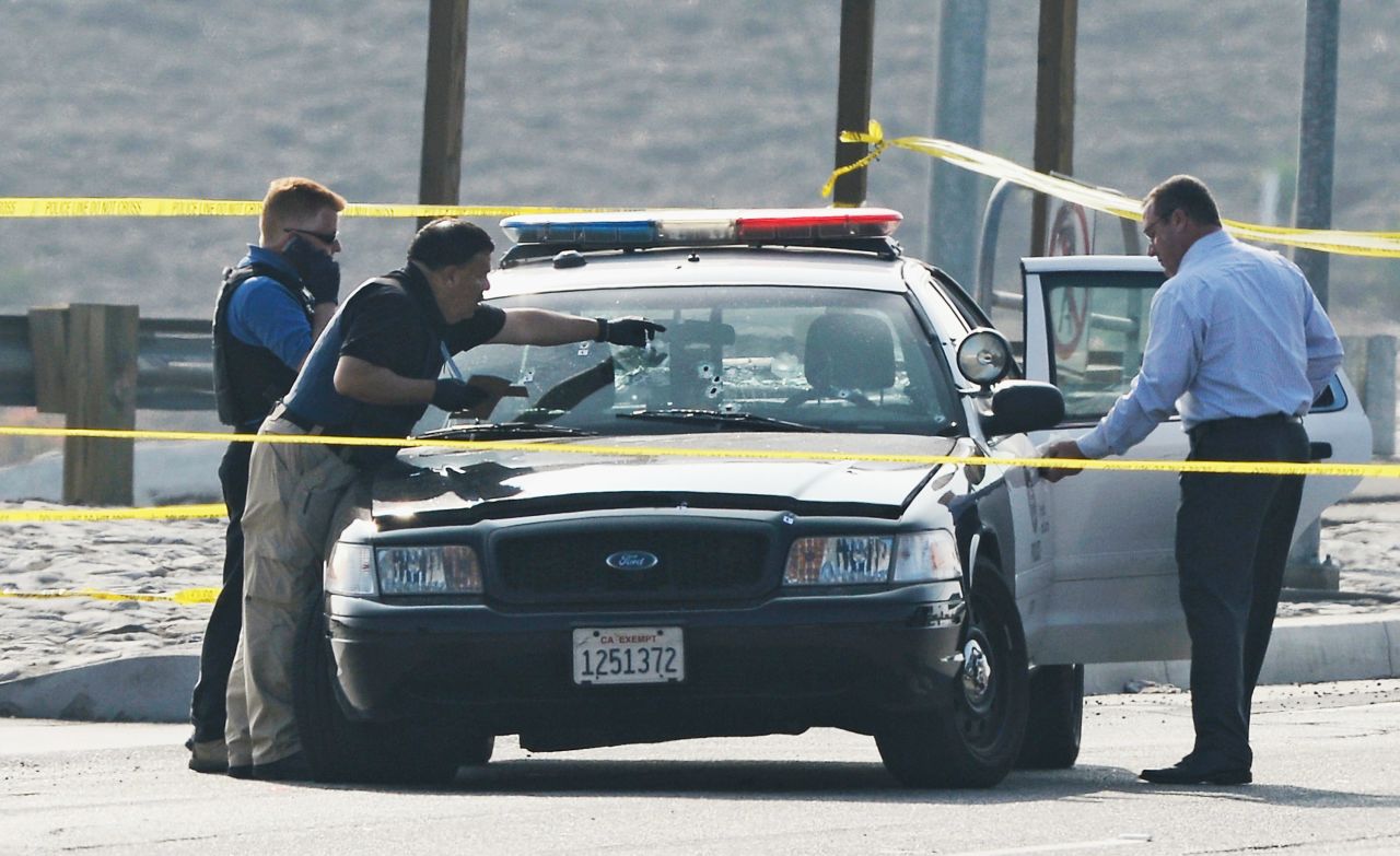 Investigators inspect a bullet-ridden squad car where a police officer was shot on Magnolia Avenue in Corona, California on February 7.