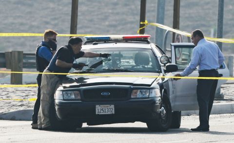Investigators inspect a bullet-ridden squad car where a police officer was shot on Magnolia Avenue in Corona, California on February 7.