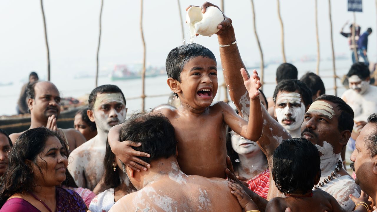 A boy reacts as water is poured over his head at the edge of the Sangam.
