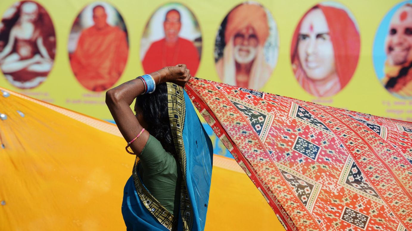An Indian Hindu devotee dries her sari in the wind as she stands near a billboard showing Hindu gurus in  Allahabad, India, on February 8.