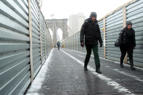 Two people carefully walk across the Brooklyn Bridge in the snow and sleet on February 8.