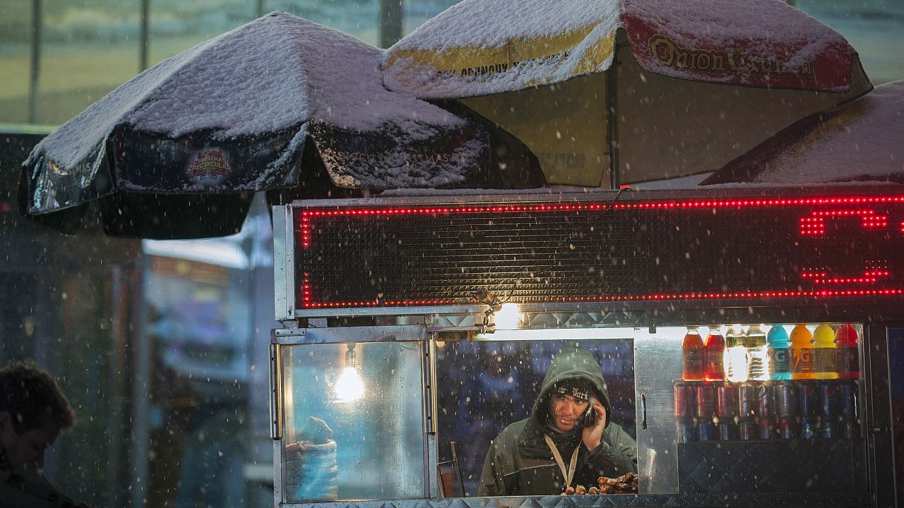 A food vendor stands under his cart as snow falls in Times Square.