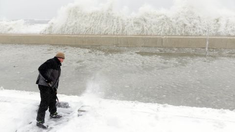 Mike Streeter shovels snow in his front yard as ocean water crashes over the sea wall just feet away on February 9 in Winthrop, Massachusetts.