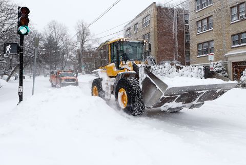 A front loader and truck drive down Warren Street in the Brighton neighborhood on Saturday in Boston. 
