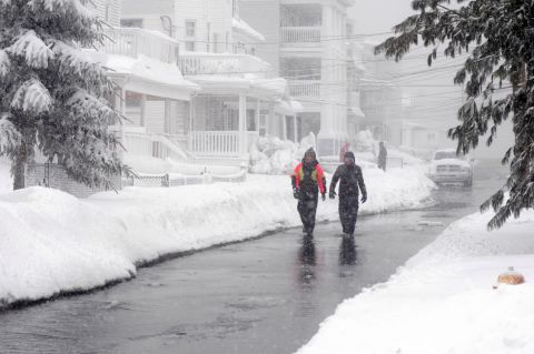 People walk along a street devoid of snow due to ocean flooding Saturday in Winthrop, Massachusetts. Coastal flooding is expected as the storm lingers into the day.