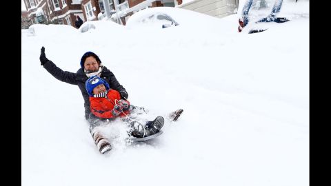 Josephine Sipayung and her son Eric, 6, sled down an empty street past snow-covered vehicles in Boston on Saturday.