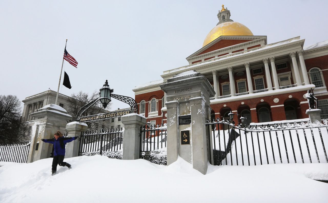A young woman jumps down from snow piled in front of the Massachusetts State House after posing for a photo in Boston on Saturday.
