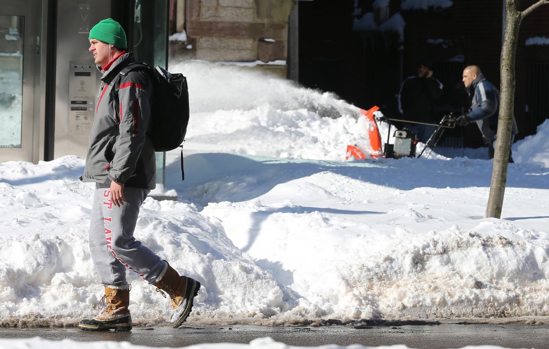 A man walks by as another clears snow from a sidewalk Saturday in the Back Bay neighborhood of Boston.