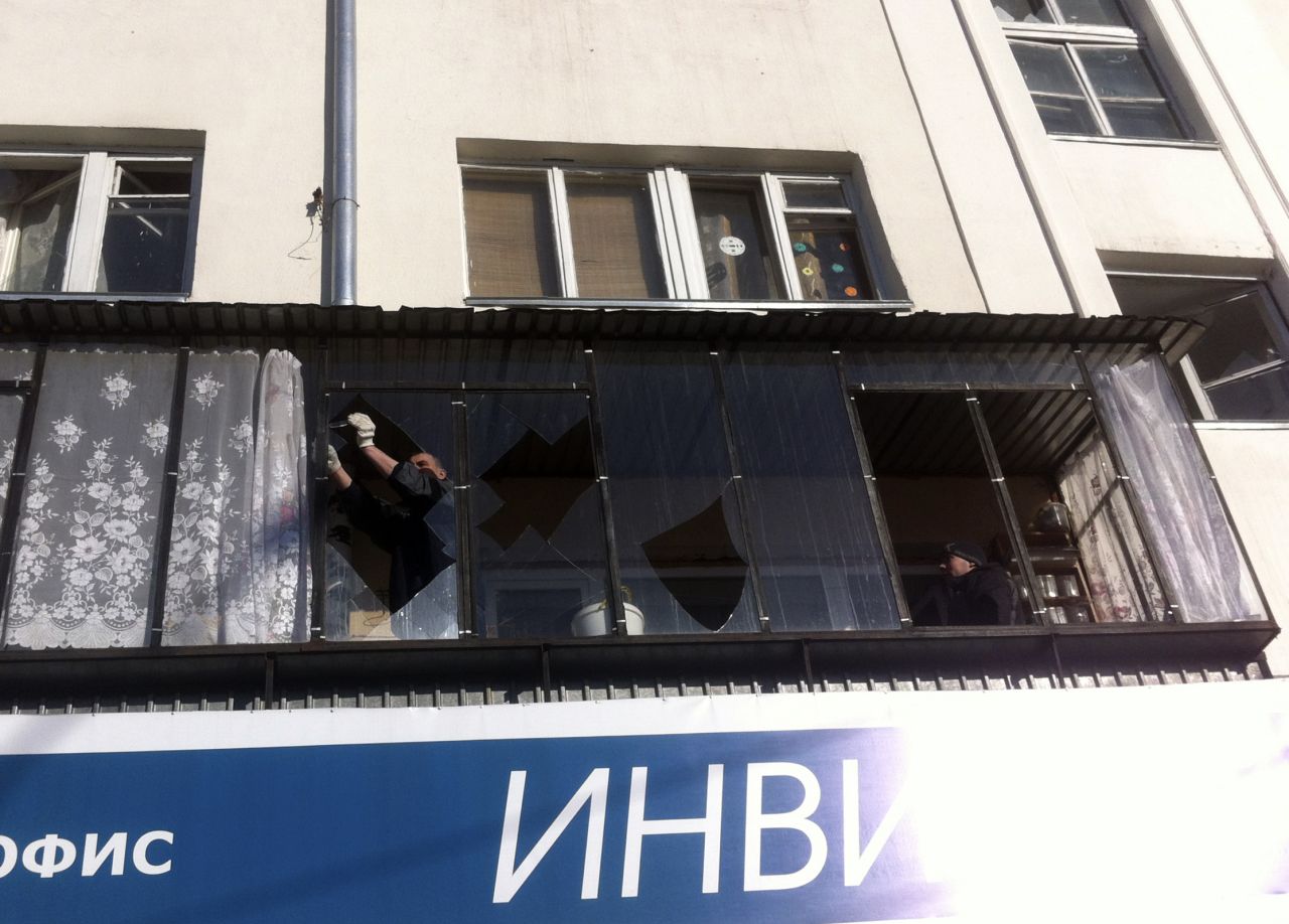 A man removes shards of glass from the frame of a broken window. 