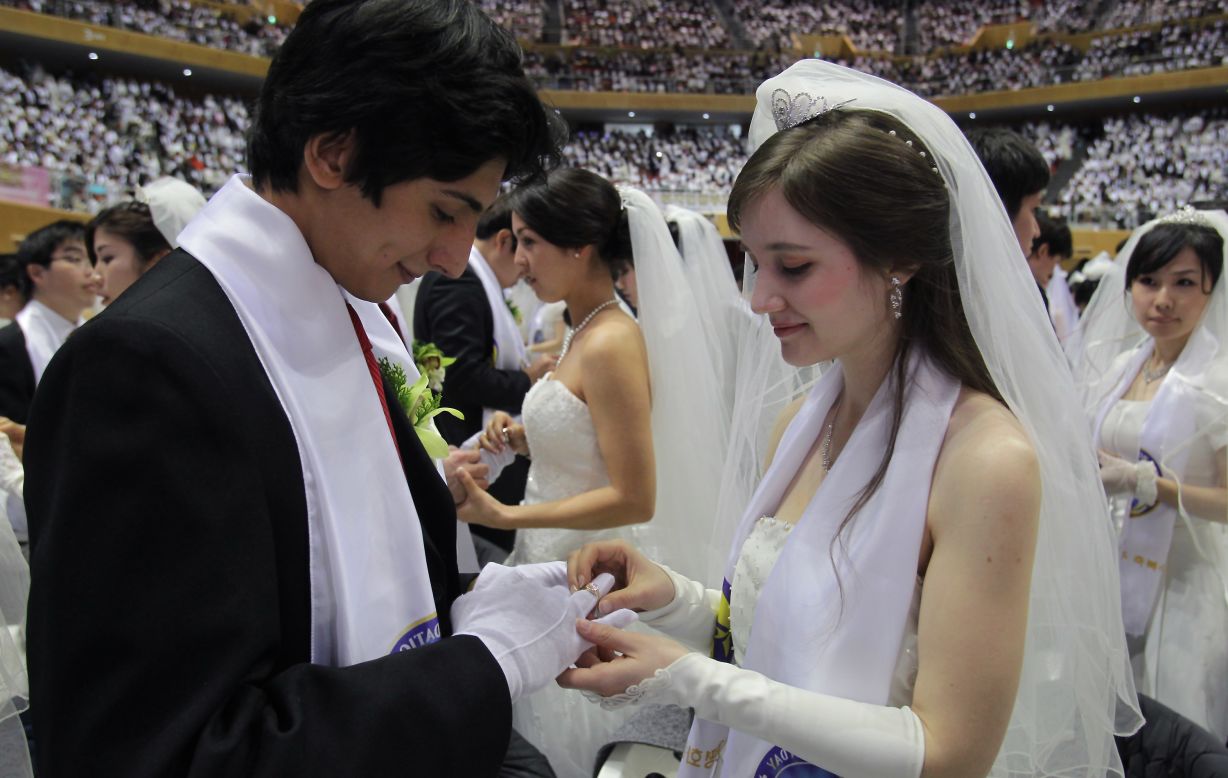 A bride puts a ring on her groom's hand.