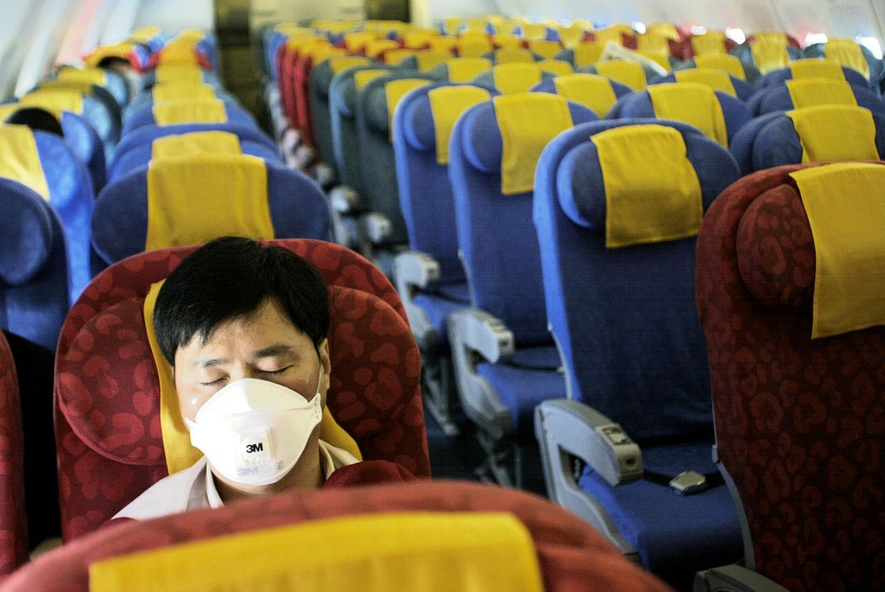 A masked passenger sleeps on an nearly empty Dragonair flight from Hong Kong to Beijing on May 21, 2003. The Hong Kong-based carrier saw passenger volumes plummet after the SARS outbreak.