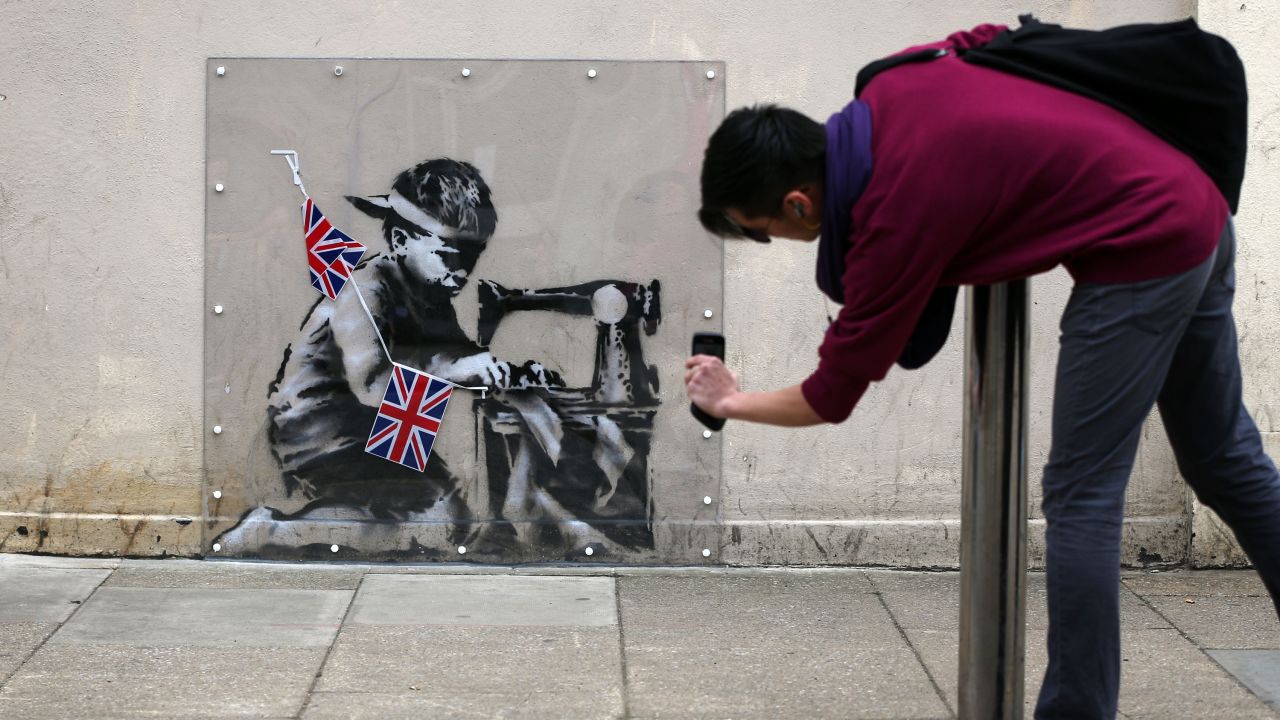  A man takes a photo of the artwork "Slave Labour," attributed to Banksy, on May 17, 2012, in London. 