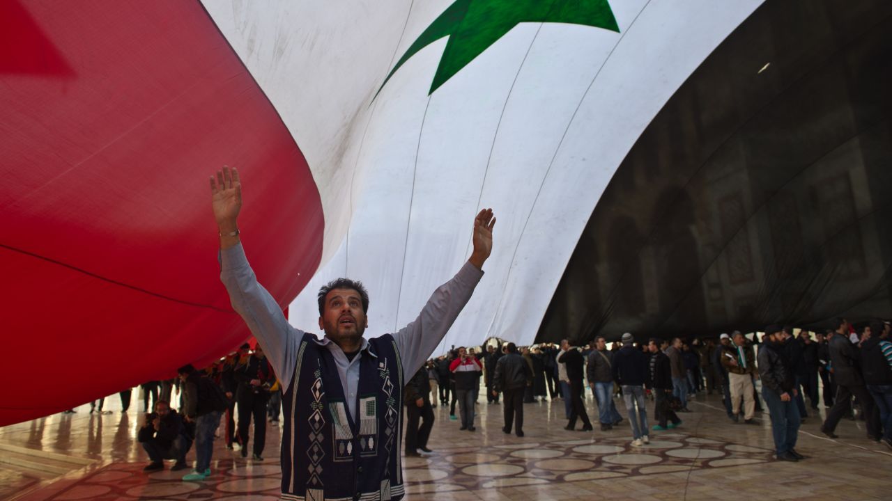 A man stands under a giant Syrian flag outside the Umayyad