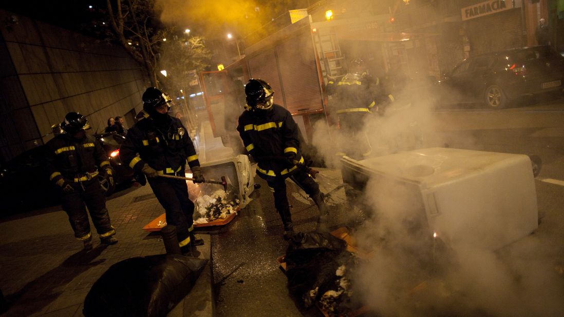Firemen extinguish a bin on fire during a riot after a march by thousands of people.
