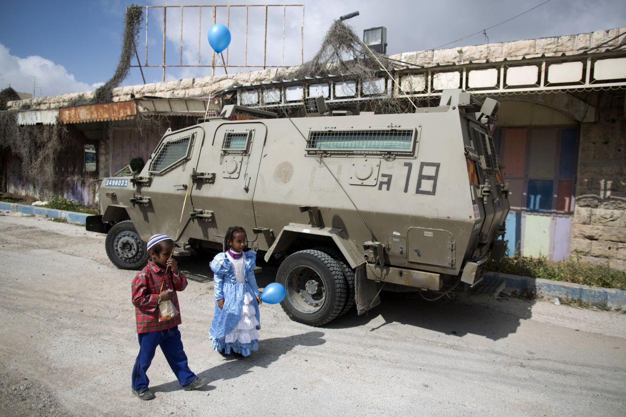 Children of Israeli settlers wearing costumes walk past an army vehicle as they celebrate the annual Purim parade in the occupied West Bank city of Hebron.