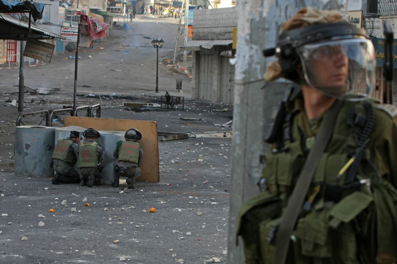 Israeli security forces take cover behind barrels during clashes with Palestinian protestors near the Israeli checkpoint in the West Bank town of Hebron on February 25, 2013.