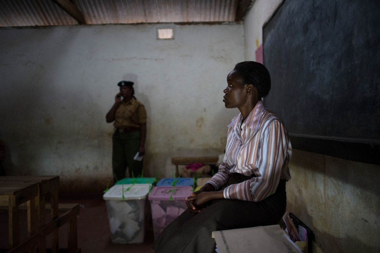 An election observer sits beside sealed ballot boxes after the close of voting at the Oloolua Primary School as voting closes.