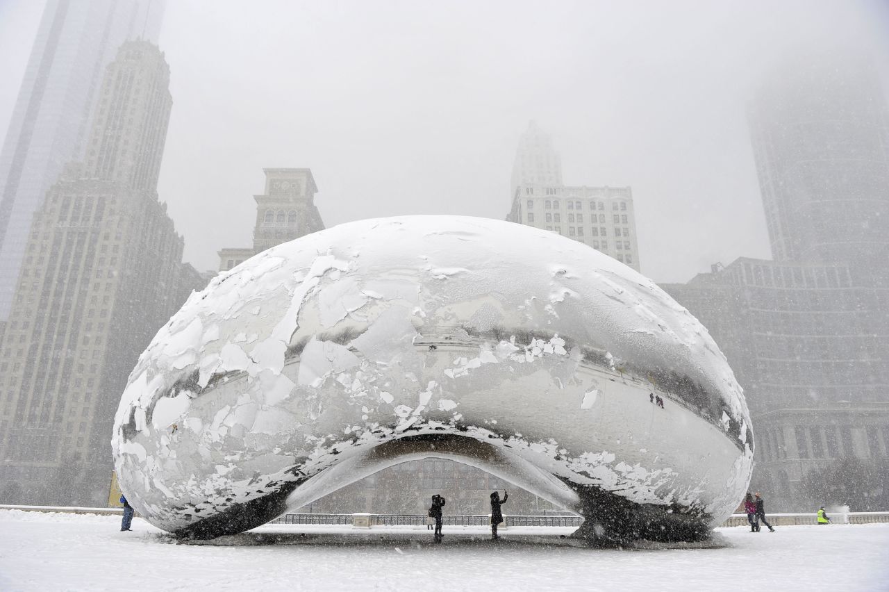 People stand under the snow-covered "Cloud Gate" sculpture, commonly known as "the bean," on Tuesday, March 5, in Chicago, Illinois.