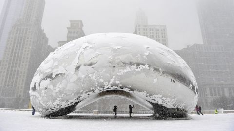 People stand under the snow-covered "Cloud Gate" sculpture, commonly known as "the bean," on Tuesday, March 5, in Chicago, Illinois.